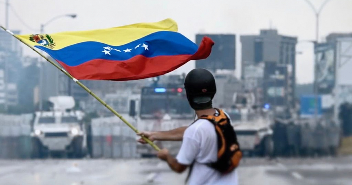 Joven venezolano ondea la bandera del país ante la presencia de policías © Wikipedia