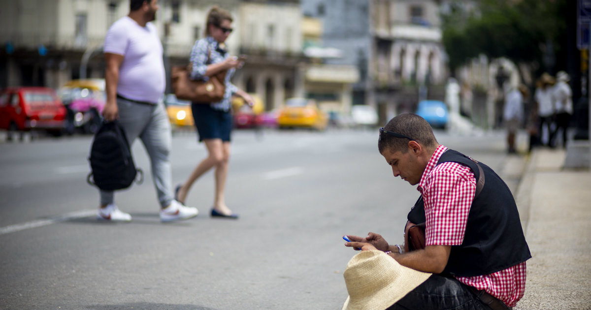 Un hombre mira su celular sentado en una calle en Cuba © Fonoma/ Fernando Medina