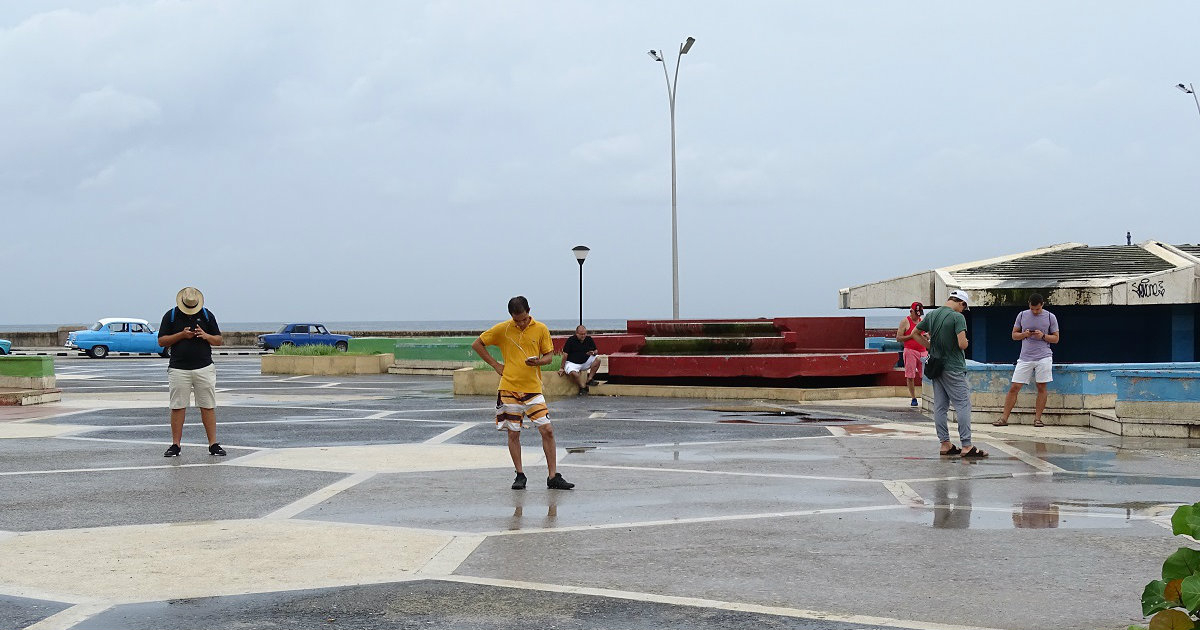 Cubanos miran sus celulares en Paseo y Malecón © CiberCuba