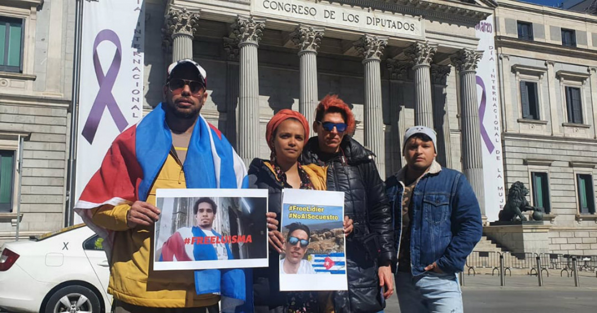 Un grupo de activistas frente al Congresos de los Diputados, en Madrid, sostienen dos fotos de los activistas Luis Manuel Otero y Lidier Hernández © Facebook/Movimiento: Acciones por la Democracia