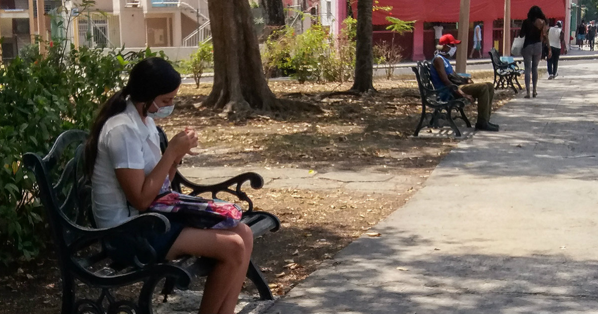 Personas con mascarillas sentadas en bancos de un parque (referencia © CiberCuba