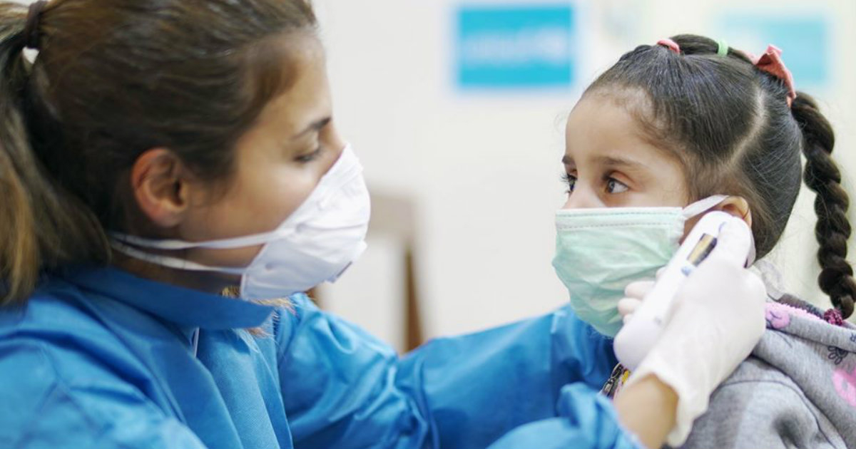 Personal sanitario coloca una mascarilla a una niña © Unicef