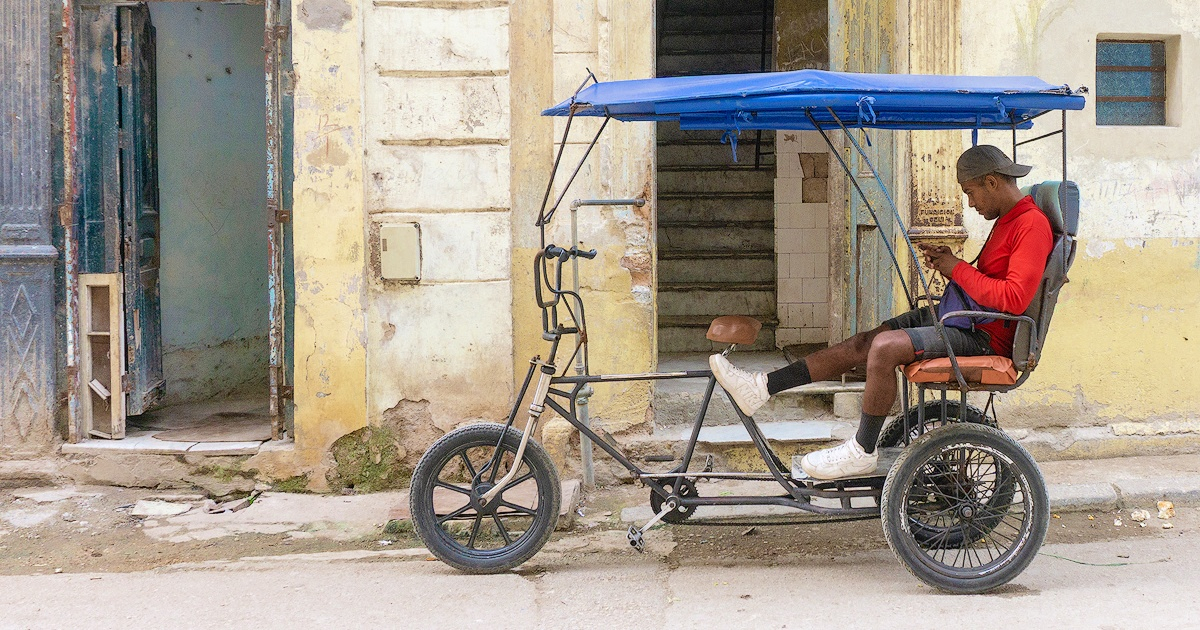 Cubano en un bicitaxi mira su teléfono celular © CiberCuba