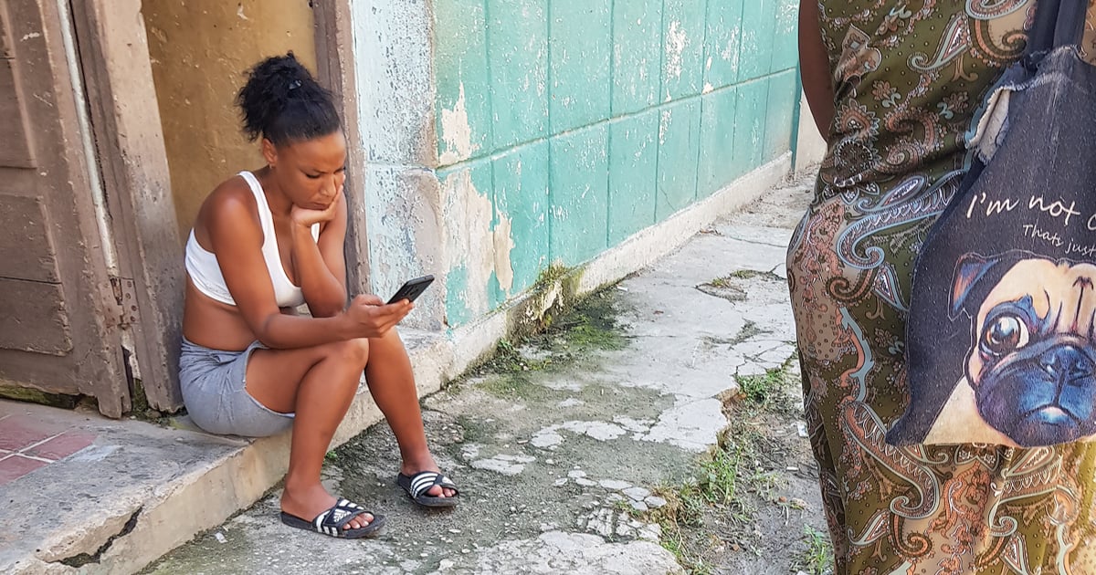 Cubana mira su celular en la puerta de su casa © CiberCuba