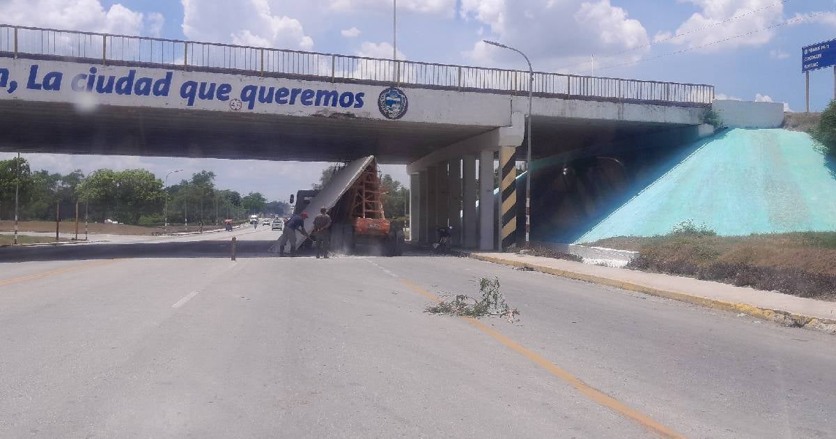 Fotografía de alta calidad del accidente de una rastra con una losa de hormigón incrustada en un puente en Holguín, Cuba, con tráfico detenido. Estilo documental y realista.