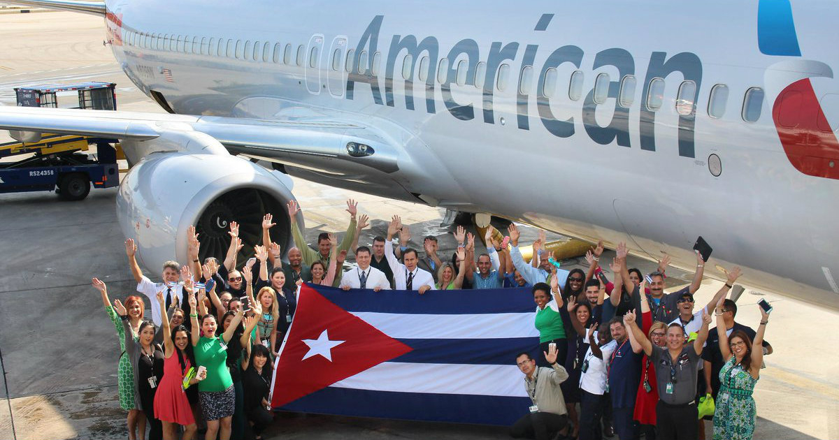 Un grupo de pasajeros cubanos posa con la bandera con un avión de fondo © 