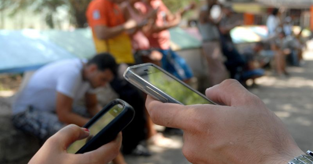 Dos ciudadanos cubanos usan su teléfono celular en una zona wifi © Escambray / Abel Rojas