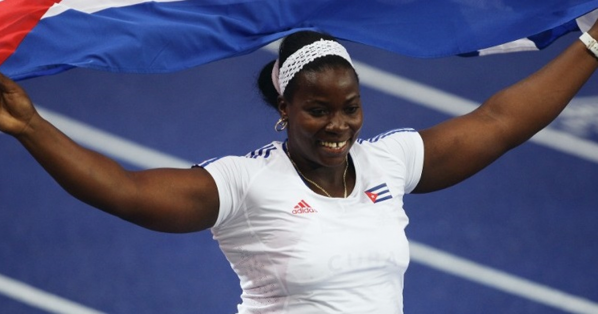 La atleta cubana Yarelis Barrios posa sonriente con la bandera cubana © Getty Images / Mark Dadswell